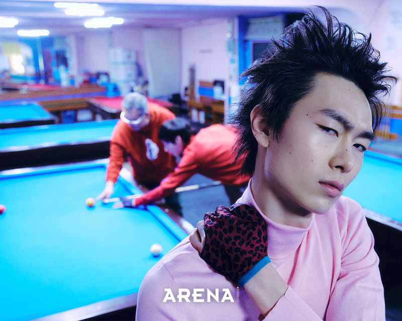 Man wearing a pink turtleneck and leopard print glove looking back at the camera in a billiards hall for Arena Homme Plus Korea.