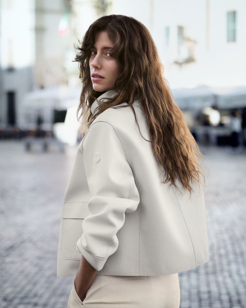 Woman with long brown hair wearing a light-coloured jacket outdoors in a public square