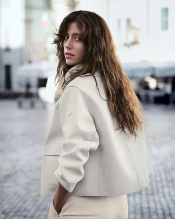 Woman with long brown hair wearing a light-coloured jacket outdoors in a public square