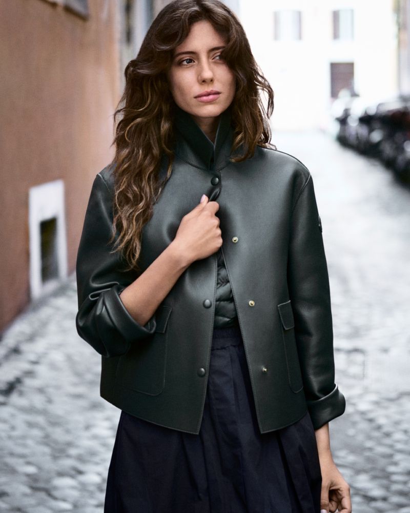 Woman wearing a dark green structured jacket on a cobblestone street for Moncler Collection Spring 2026.