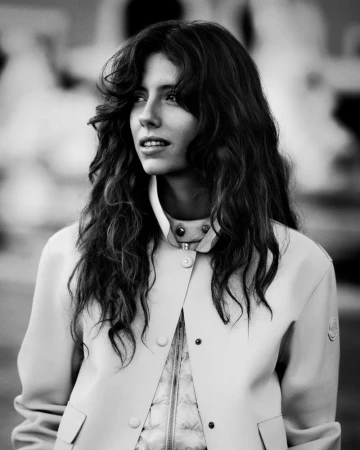 Monochrome portrait of a woman with long wavy hair wearing a snap-button jacket for Moncler Spring 2026.
