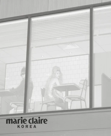 Models seated inside a restaurant viewed through large exterior windows in a black and white editorial photograph