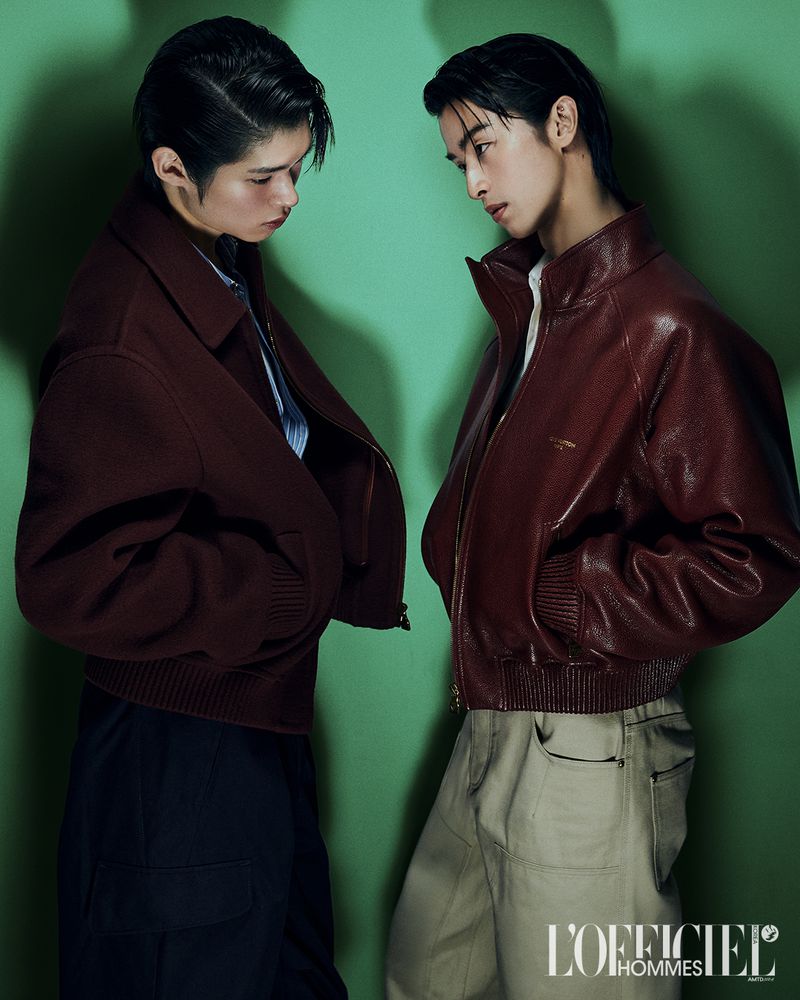 Two male models posing against a green backdrop for L'Officiel Korea, wearing leather jackets and cargo trousers.