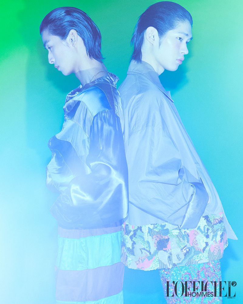 Two male models standing back-to-back in profile against a gradient blue and green background for L'Officiel Korea Duo project.