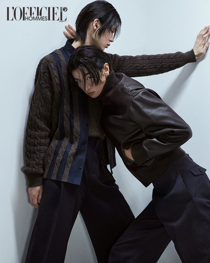 Two models posing against a light grey wall for L'Officiel Korea, wearing dark layered knitwear and leather jackets.