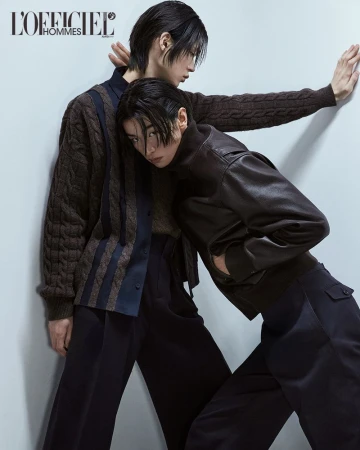 Two models posing against a light grey wall for L'Officiel Korea, wearing dark layered knitwear and leather jackets.