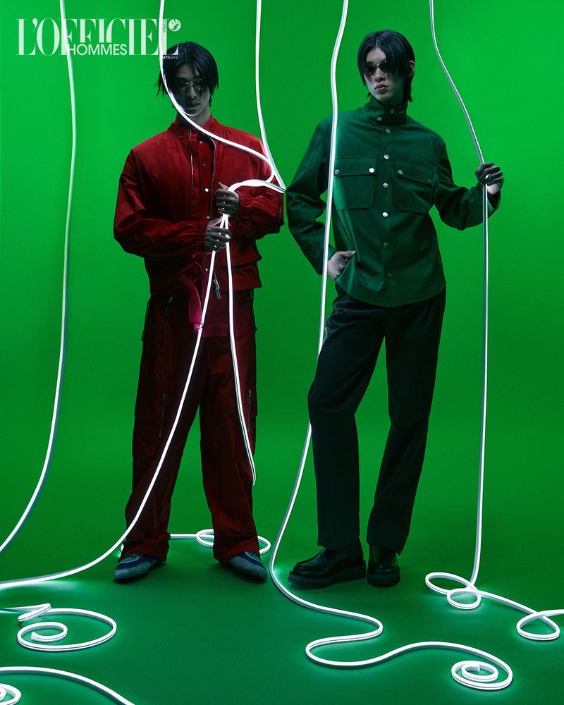 Two male models posing on a green backdrop surrounded by glowing white neon string lights for L'Officiel Korea Duo project.