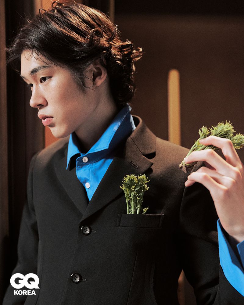 Model wearing a black suit and vibrant blue shirt with green herbs in pocket for GQ Korea