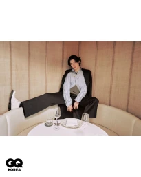 Model seated inside a restaurant booth with one foot propped up on the cushion, wearing a black blazer and wide trousers.