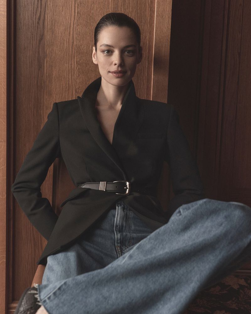 Model wearing a black blazer and blue jeans against a dark wooden interior paneling background for Veronica Beard Spring 2026.
