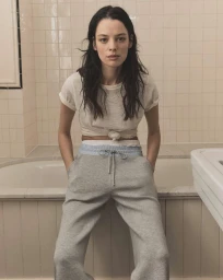 Model wearing a white t-shirt and grey sweatpants sitting in front of a tiled bathtub for Veronica Beard