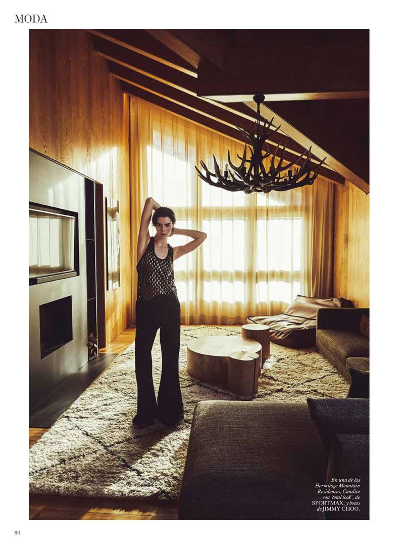 Model standing with hands behind head in a luxury wooden chalet living room for Vogue Espana