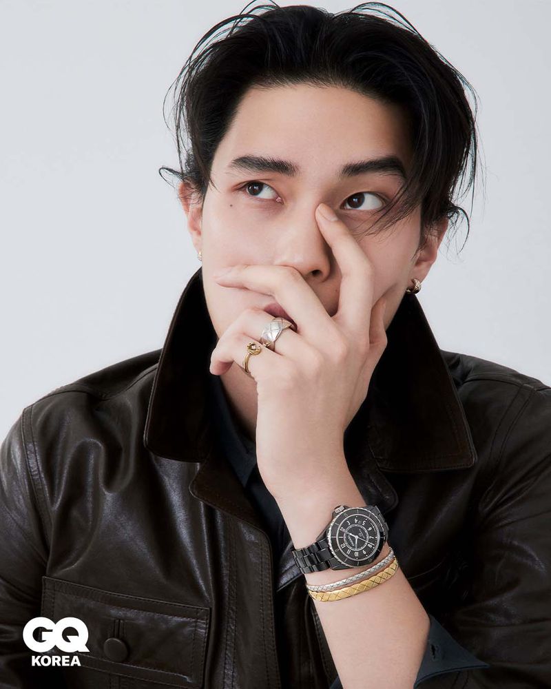 Close-up portrait of Jinyeong Pak wearing a brown leather jacket and watch, with hand near face against a white background for GQ Korea.