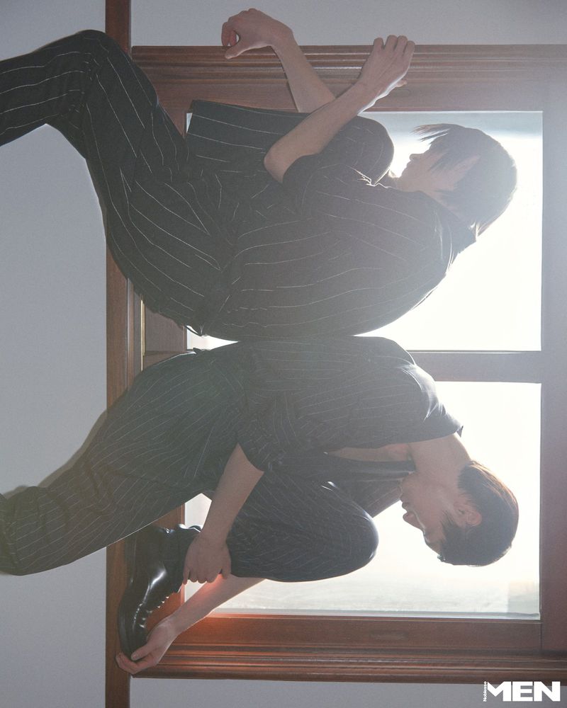Model in dark pinstripe suit posing near a window for Noblesse Korea photographed by Sin ae Kim