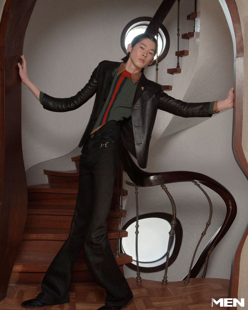Model leaning against a curved wooden doorway in a stairway wearing a leather blazer and dark trousers for Noblesse Korea.