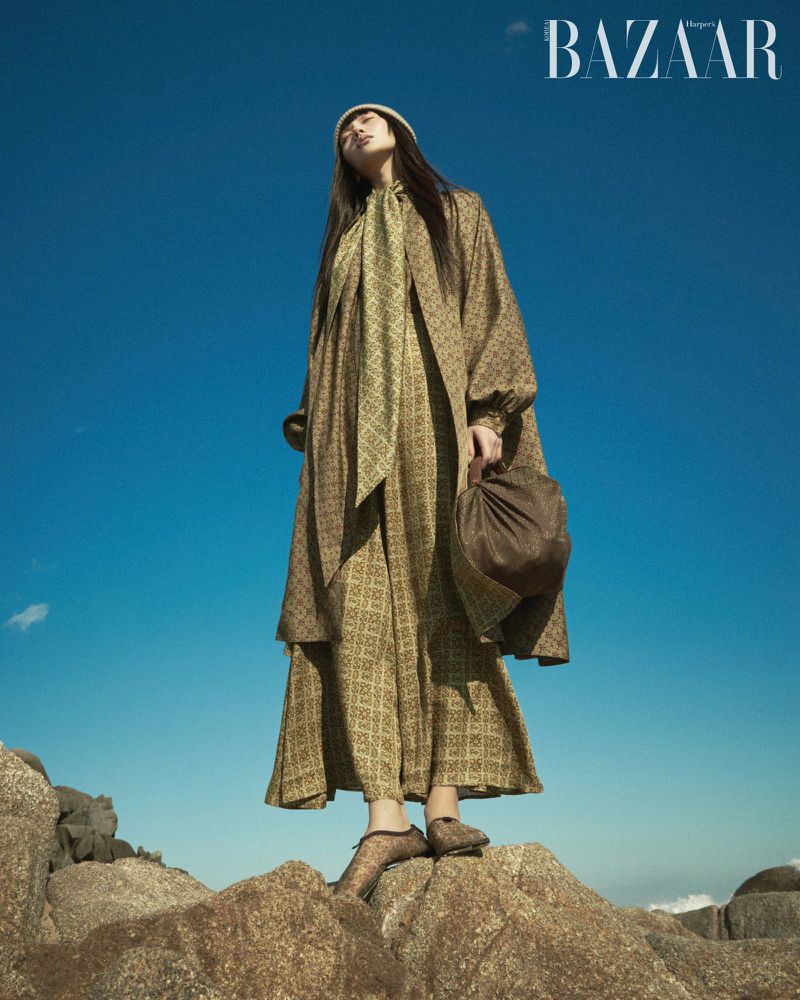 Model in patterned coat standing on rocks against a clear blue sky for Harper's Bazaar Korea