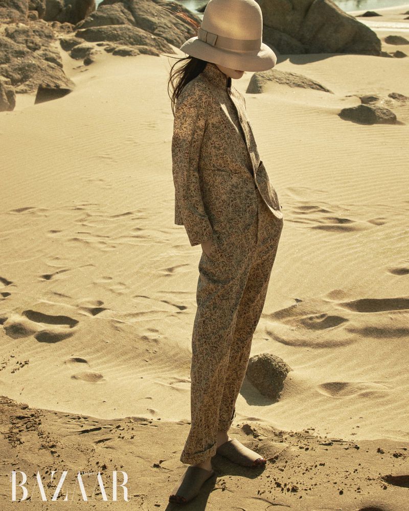 Model wearing a wide-brimmed hat and patterned pantsuit standing on sand dunes for Harper's Bazaar Korea