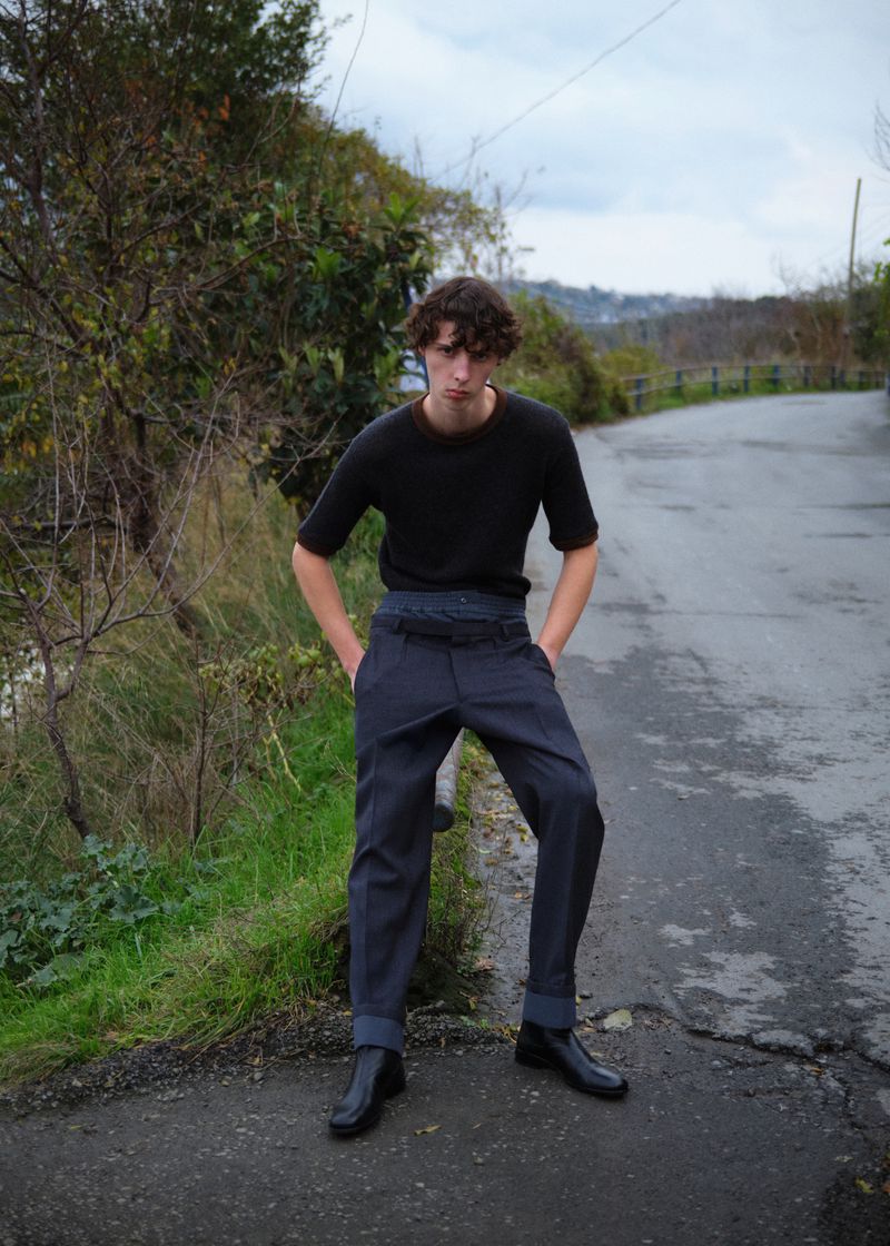 Young male model standing on a rural asphalt road wearing a dark t-shirt and grey trousers for L'Officiel Hommes Turkey.