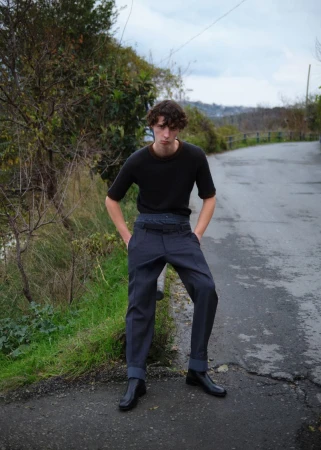Young male model standing on a rural asphalt road wearing a dark t-shirt and grey trousers for L'Officiel Hommes Turkey.