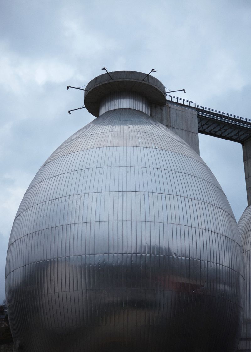 Large bulbous metallic industrial tank structure under an overcast sky with a connecting walkway