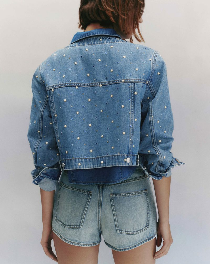 Model from behind wearing a studded denim jacket and denim shorts against a neutral background