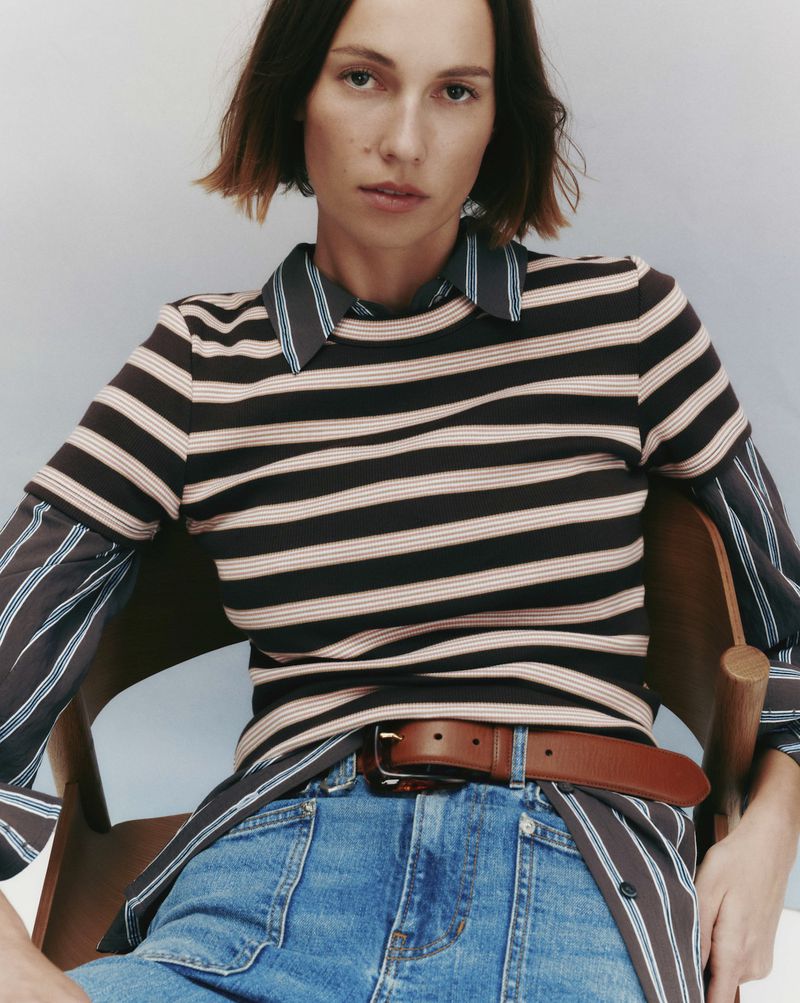 Model Mali Koopman wearing a striped sweater and denim jeans seated on a wooden chair for Veronica Beard