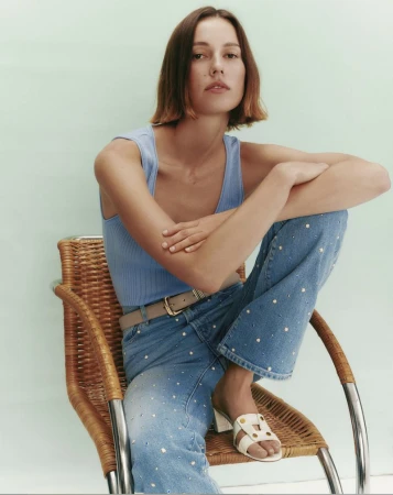 Model Mali Koopman seated in a wicker chair wearing a blue tank top and embellished jeans for Veronica Beard
