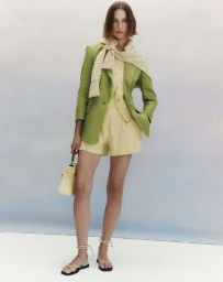 Model Mali Koopman in green blazer and yellow shorts holding a handbag against a seamless background