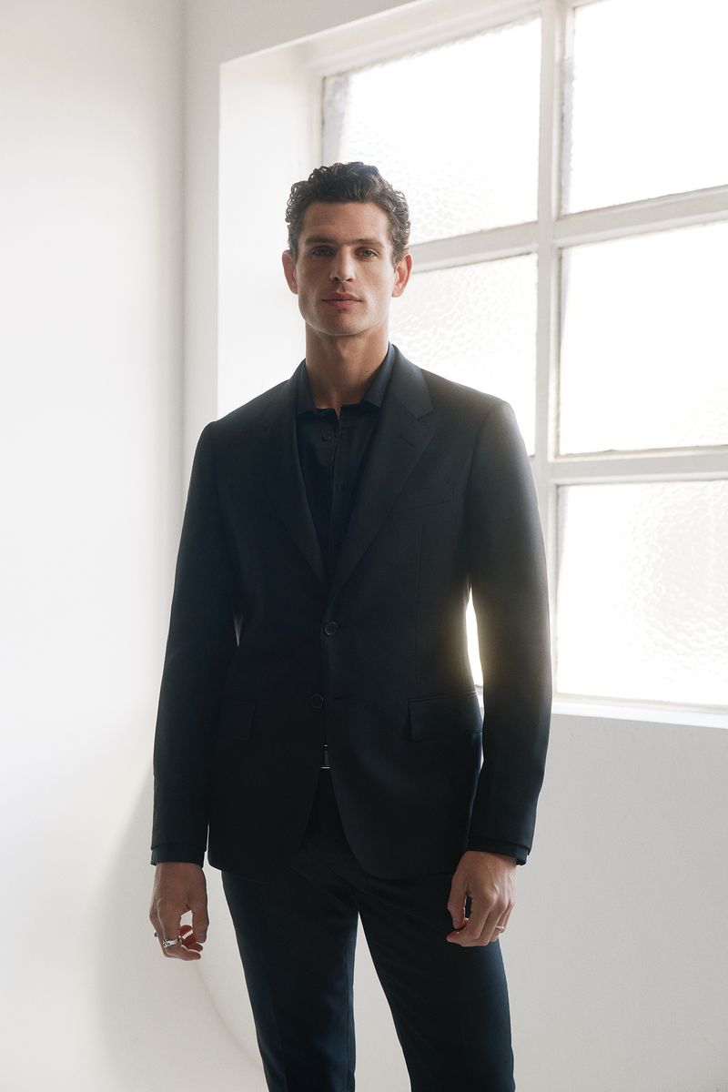 Male model in a dark suit standing against a bright window for Calibre AW26 lookbook