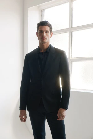 Male model in a dark suit standing against a bright window for Calibre AW26 lookbook