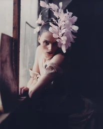 Model wearing a feathered headpiece leaning near a window in a moody editorial portrait by Antonino Cafiero