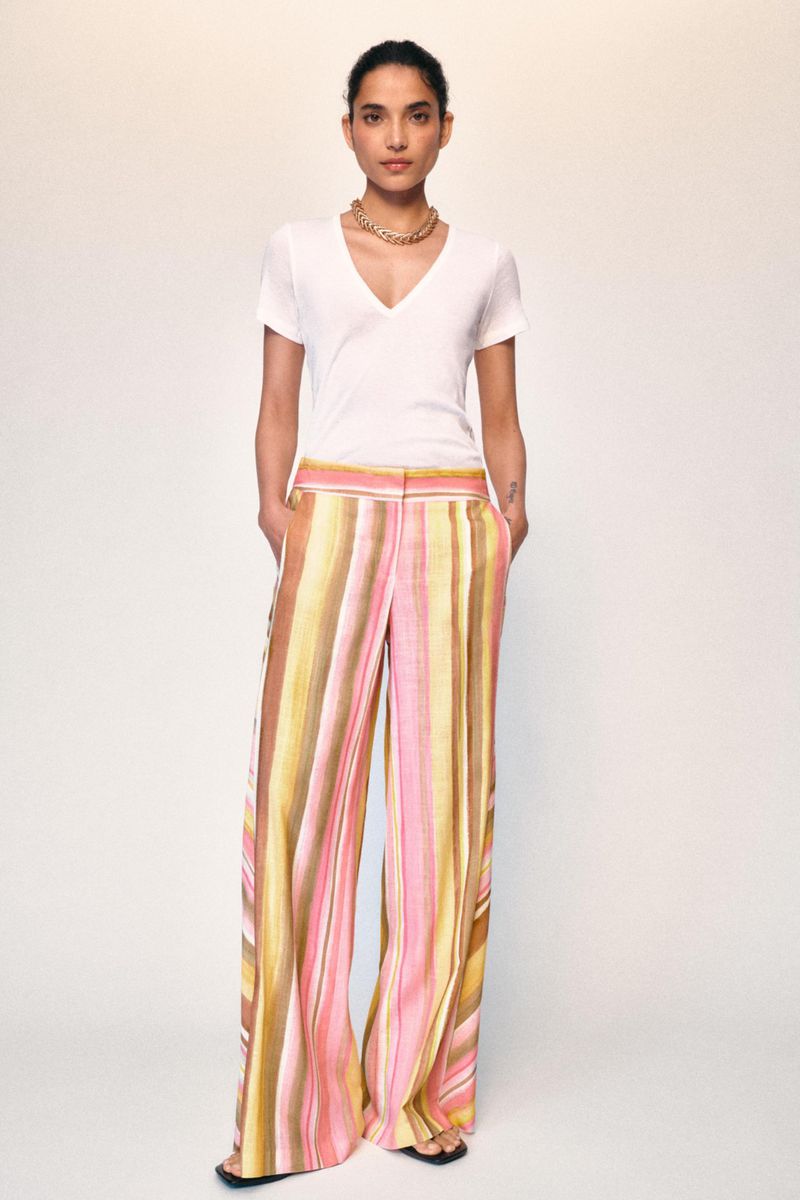 Model wearing a white v-neck t-shirt and striped trousers posing against a plain background