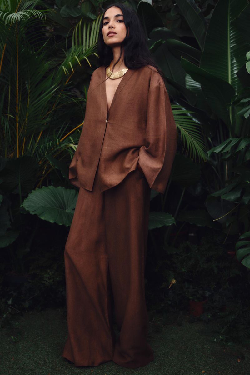 Model wearing a brown linen suit standing amidst lush green tropical foliage
