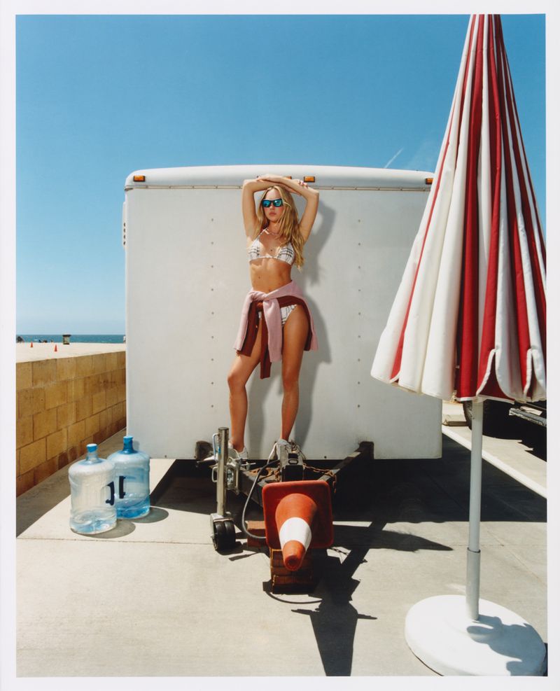 Model Lila Moss in a bikini and sunglasses posing on a trailer by the beach for Who What Wear
