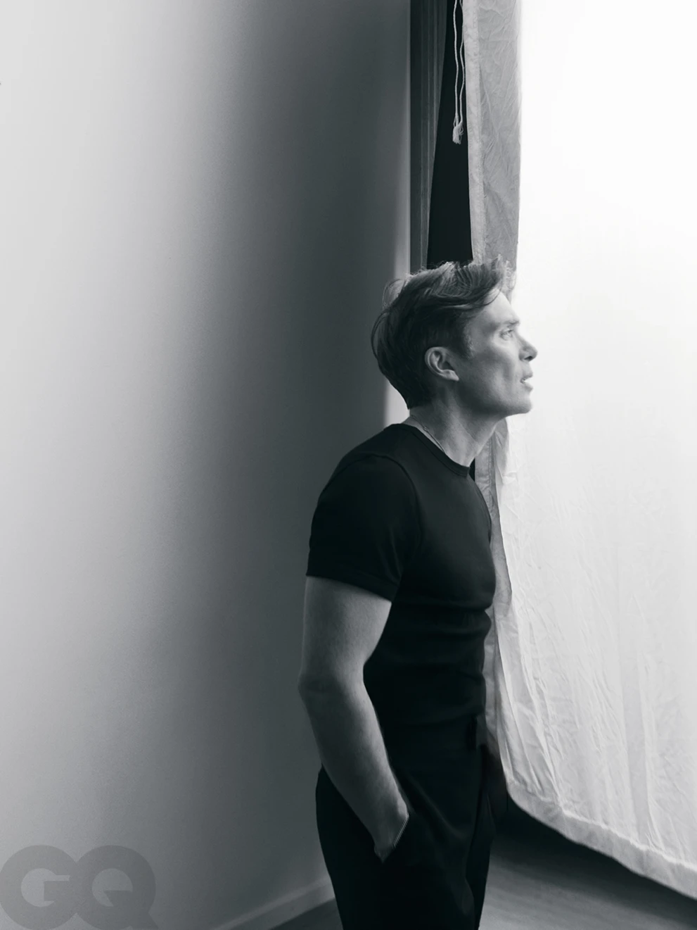 Monochrome portrait of actor Cillian Murphy wearing a black t-shirt while standing near a bright window for GQ Poland