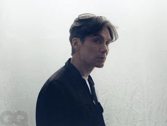 Actor Cillian Murphy looking over his shoulder in a black zip-up jacket against a creased white backdrop.