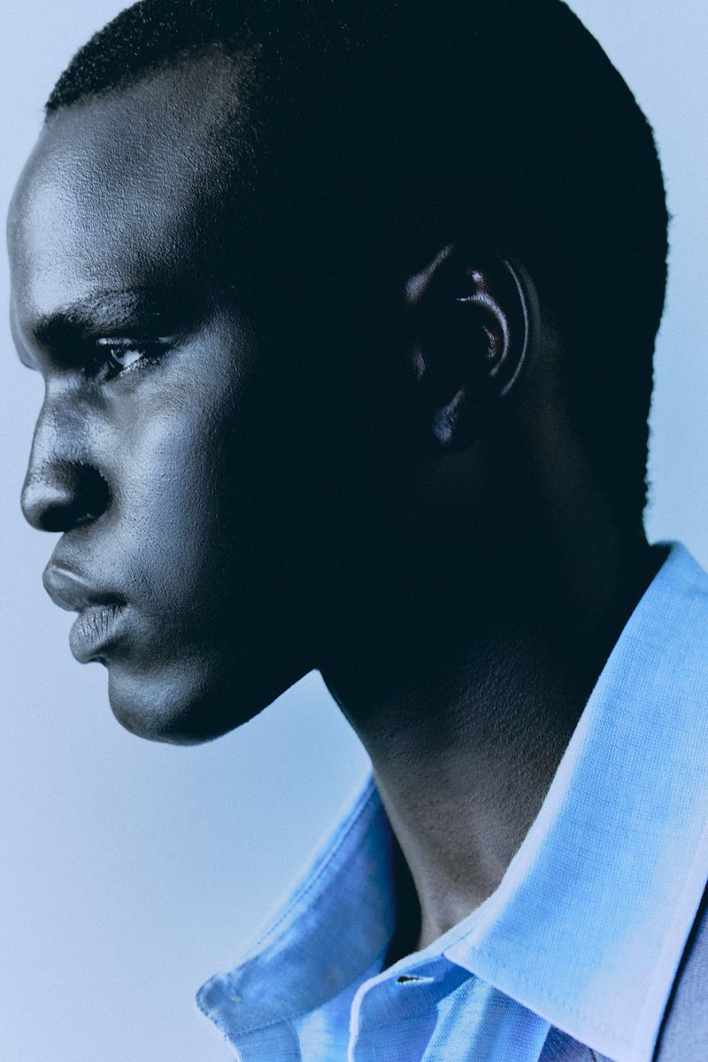 Close-up of an adult African male in a light blue collared shirt against a light blue background in a portrait-style fashion shot.