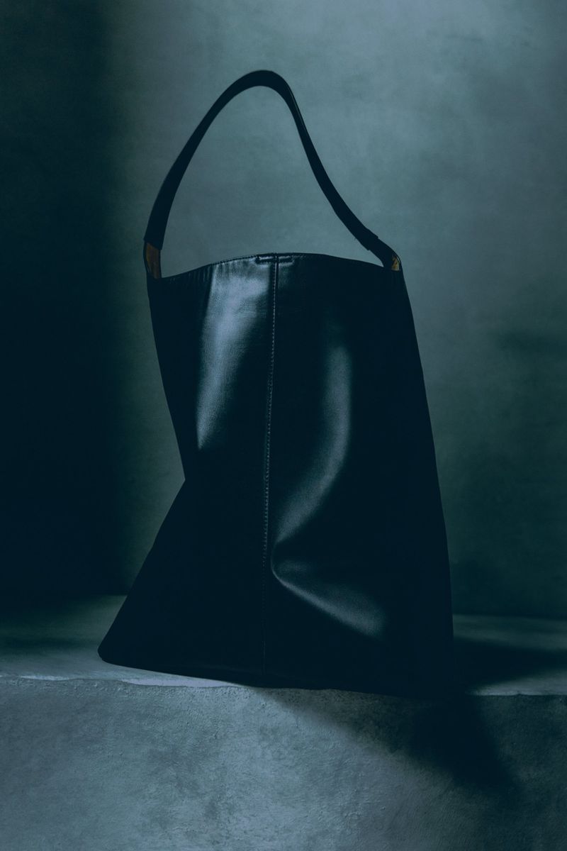 Elegant studio shot of a dark blue leather tote bag with matching handle, set against a deep, moody background with subtle texture.