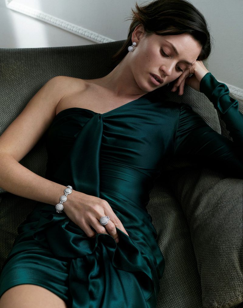 Model in green satin dress reclining on an armchair wearing diamond jewelry for Marco Valente High Jewelry Campaign