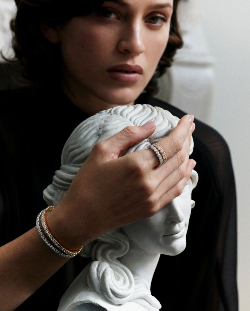 Close-up portrait of a woman wearing diamond rings and bracelets posing with a white classical bust