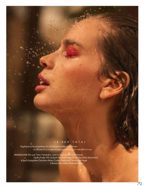 Fashion close-up portrait of a woman with red eye makeup and wet hair, illuminated by golden light with water droplets in the foreground.