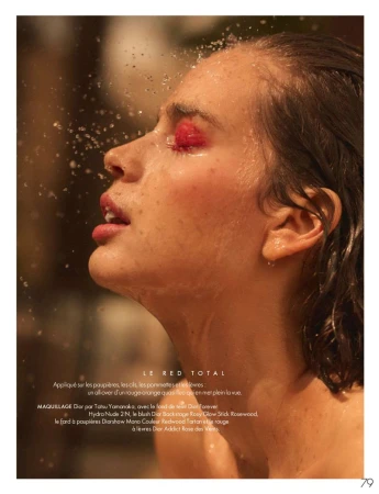 Fashion close-up portrait of a woman with red eye makeup and wet hair, illuminated by golden light with water droplets in the foreground.