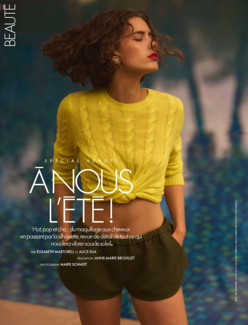 Editorial fashion shot of a young woman with curly hair, wearing a yellow sweater and green shorts, posing outdoors with closed eyes.
