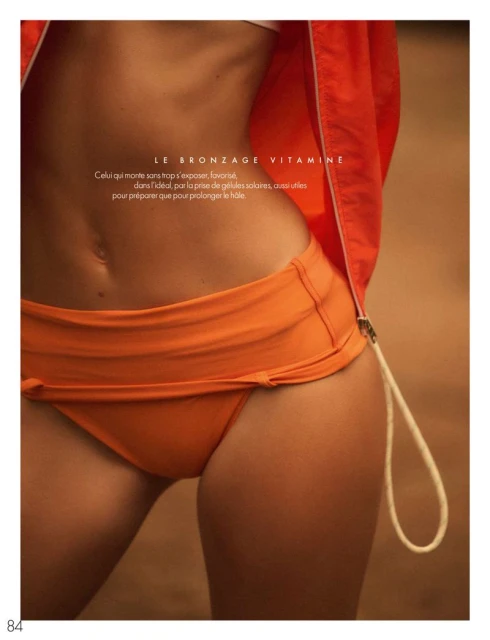 Torso of woman in orange bikini bottom with a jacket around her waist, tanned skin, and sunlight, fitness and fashion photography.