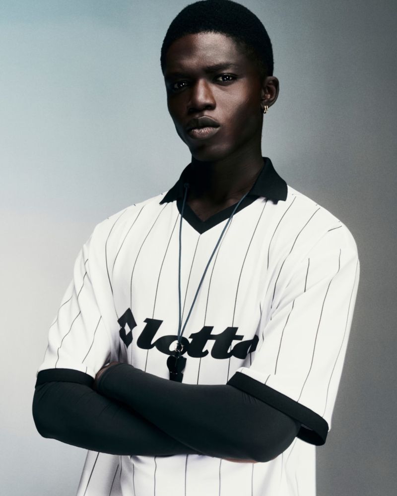 Portrait of a young adult male wearing a white sports jersey with black pinstripes and the Lotto logo, against a muted grey backdrop.