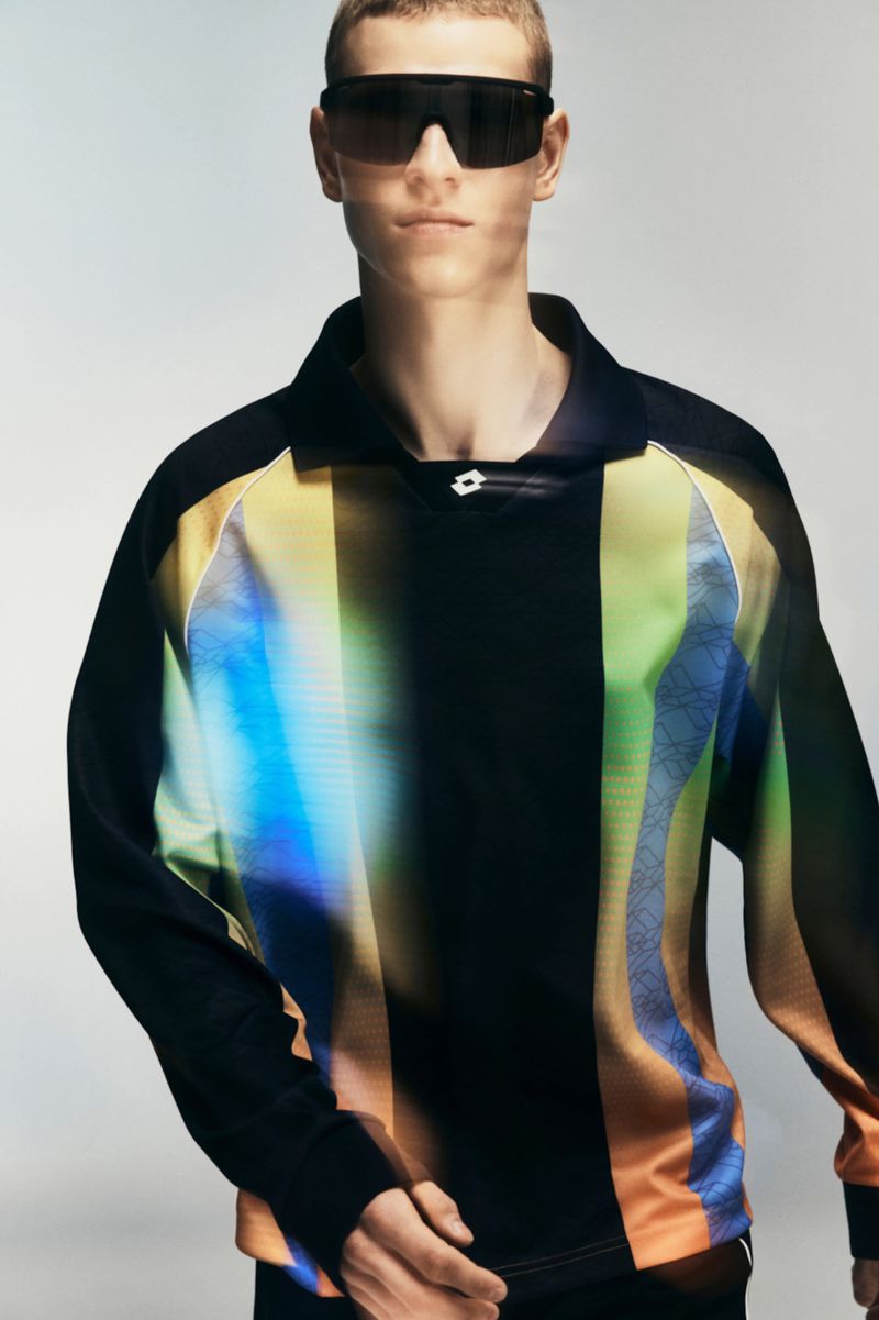Model wearing dark wrap-around sunglasses and a colour-blocked long-sleeve polo shirt against a grey seamless background