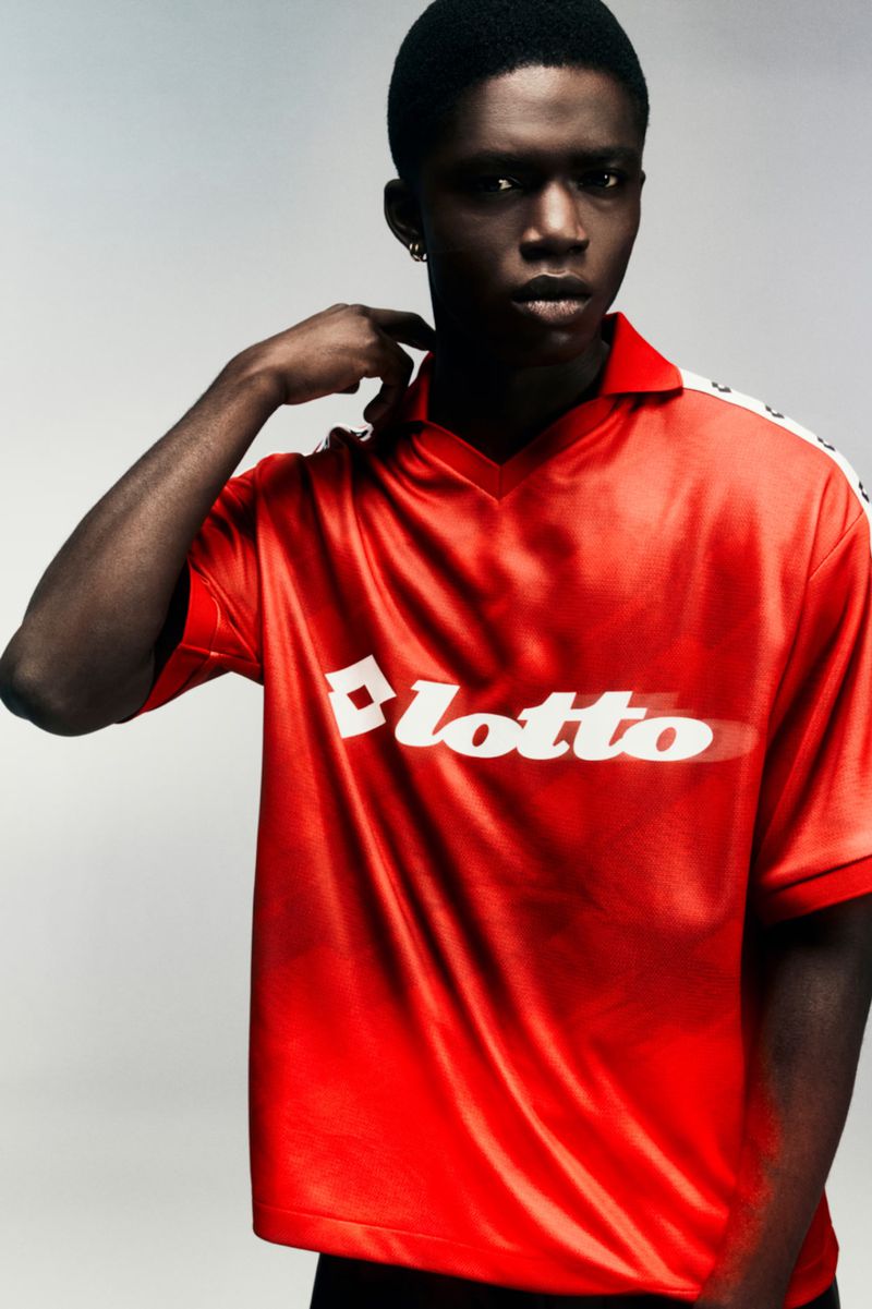 Model Jeremiah Berko Fourdjour wearing a red Lotto jersey with white branding against a grey background.