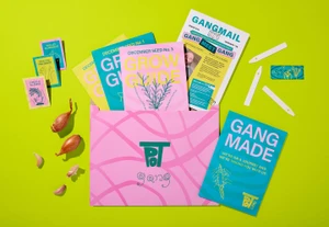 Flat lay of Pot Gang brand identity package with pink envelope, seed packets, grow guides, and fresh shallots on a vibrant green background.