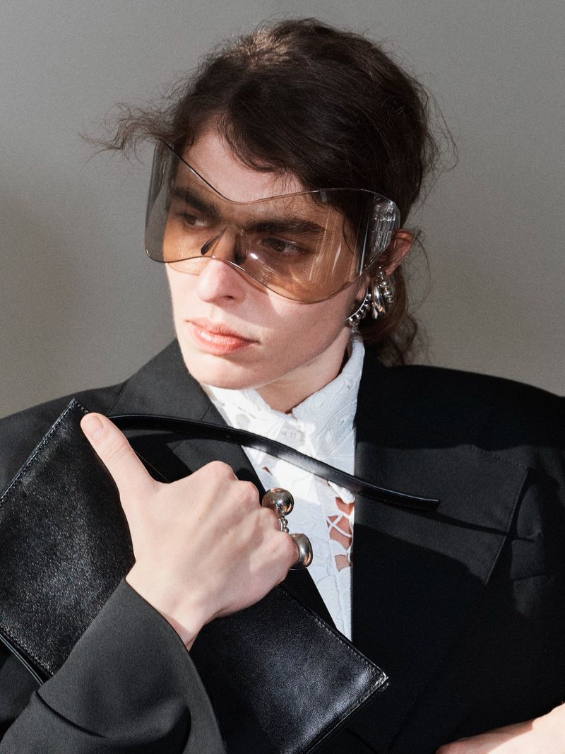 Model wearing dark tinted visor sunglasses, a black blazer, and holding a black handbag for Beaufille S/S 26 campaign.