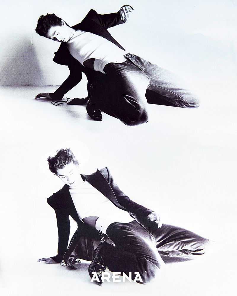 A male fashion model poses in two different kneeling positions in a monochrome fashion photograph wearing a suit and top indoors.